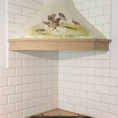 Handcrafted corner cooker hood with dynamic birds motif.
